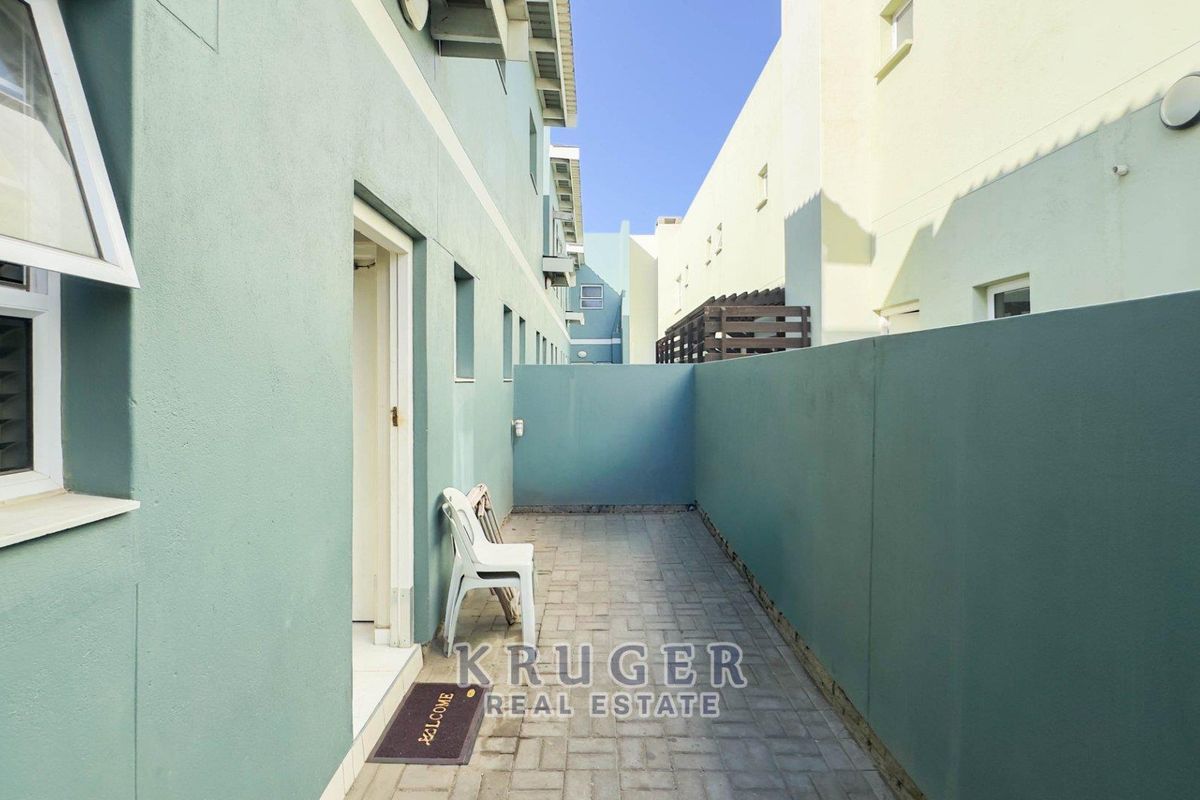 A narrow paved exterior courtyard or side passage between townhouse units, featuring painted masonry walls and a functional access door.