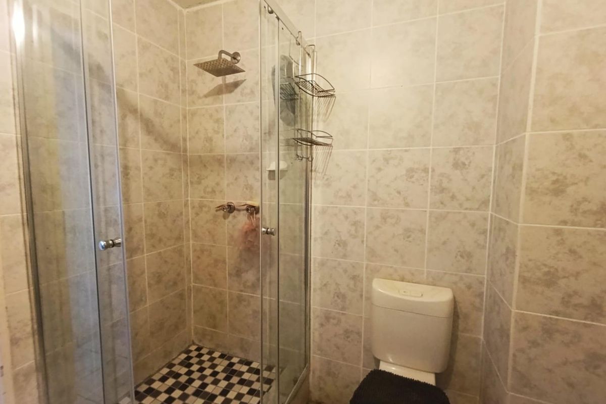A functional bathroom featuring a glass-enclosed shower with a rainfall showerhead and a standard toilet, finished with neutral wall tiling.