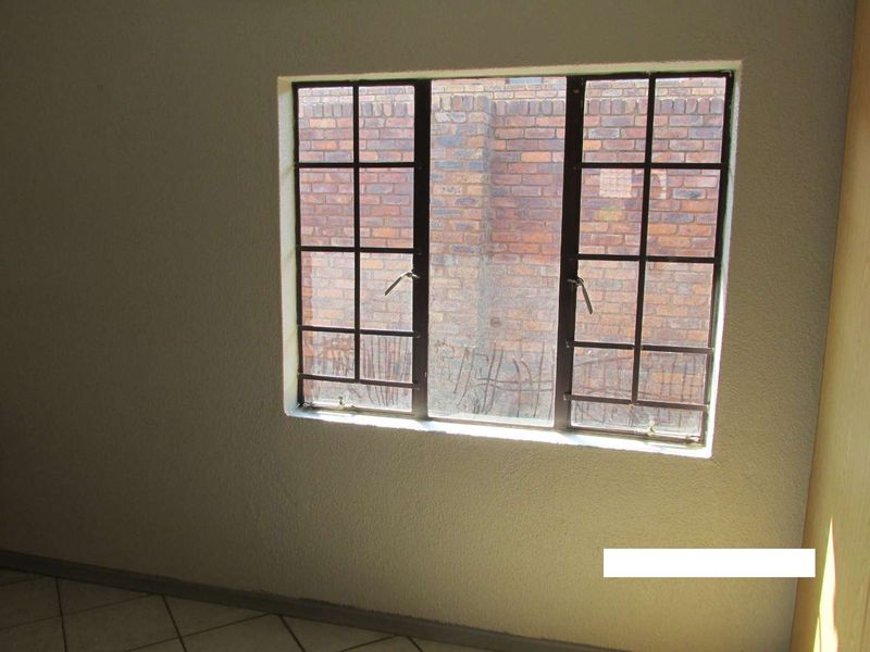 An empty bedroom featuring tiled flooring and a steel-framed window with integrated security burglar bars.