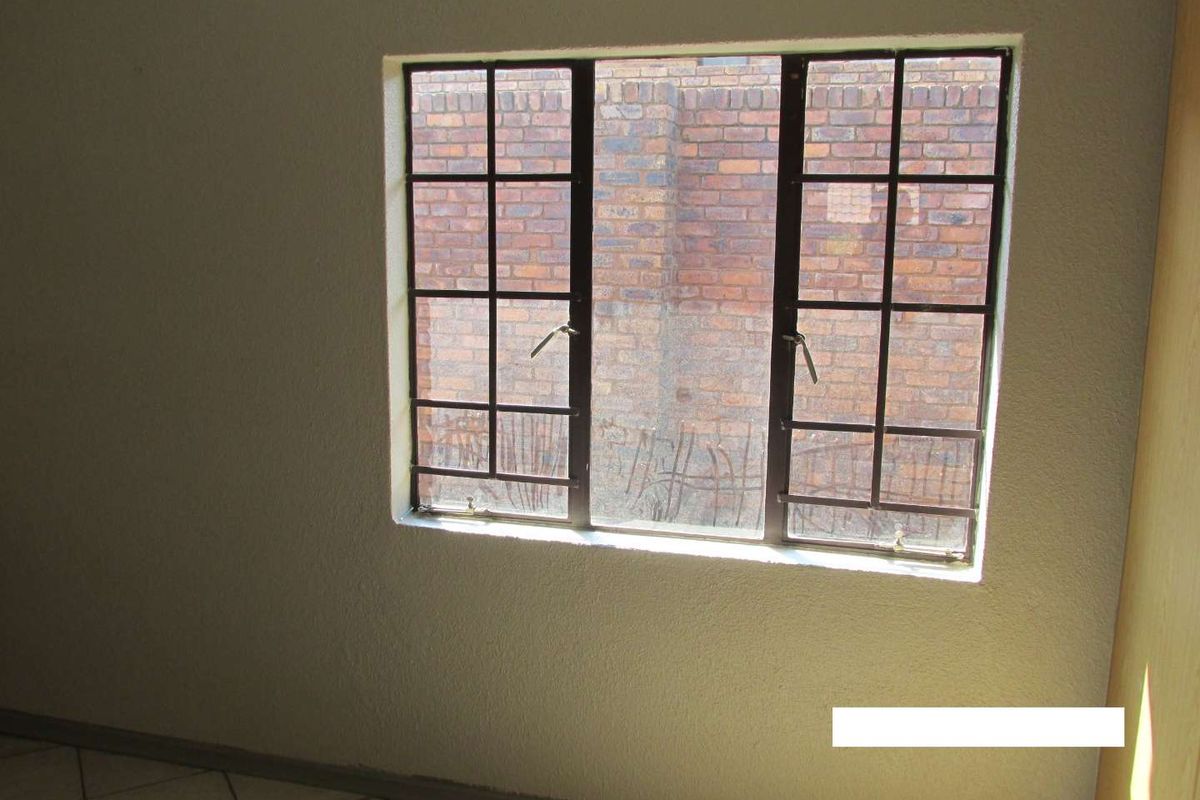 An empty bedroom featuring tiled flooring and a steel-framed window with integrated security burglar bars.