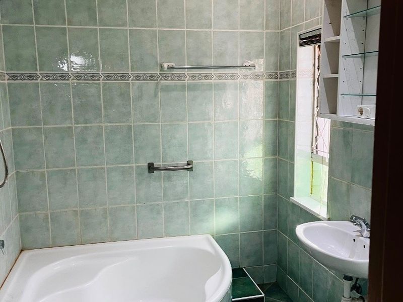 A compact bathroom featuring a corner bathtub, wall-mounted basin, and floor-to-ceiling tiled finishes, offering a functional space ready for modernization.