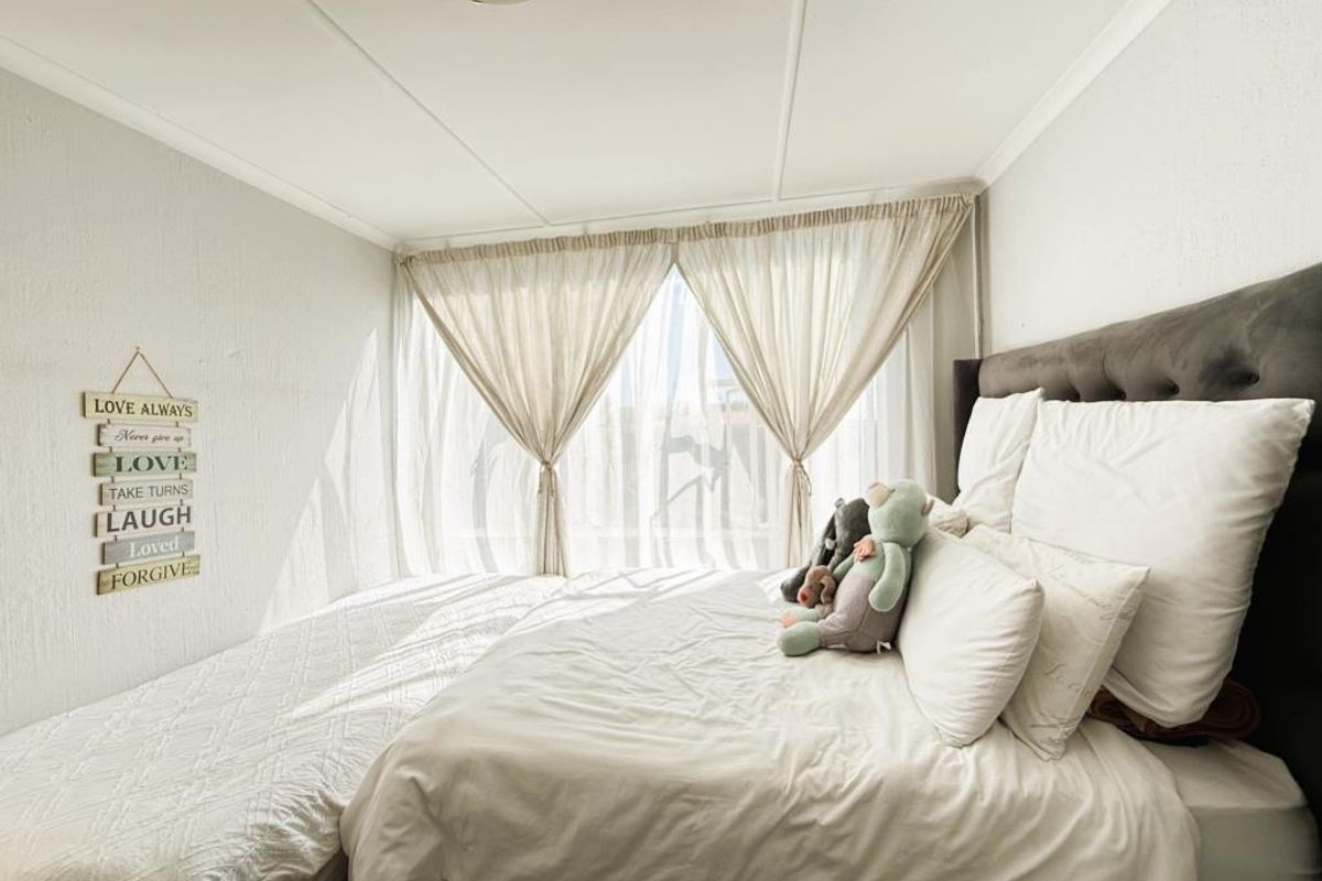 A bright bedroom featuring a large window with sheer curtains and a neutral color palette.