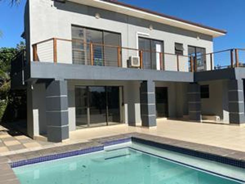 Rear view of a two-story house featuring a swimming pool, tiled patio area, and an upper-level balcony with sliding door access.