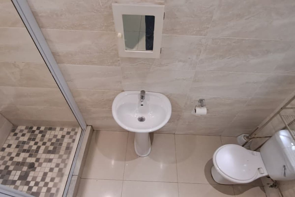 A compact bathroom featuring a glass-enclosed shower, pedestal basin, and toilet with neutral wall and floor tiling.