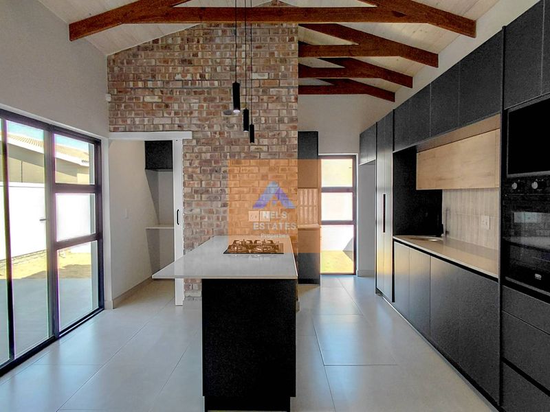 Modern kitchen featuring an exposed brick wall, timber roof trusses, a central island with a gas hob, and sleek dark cabinetry.