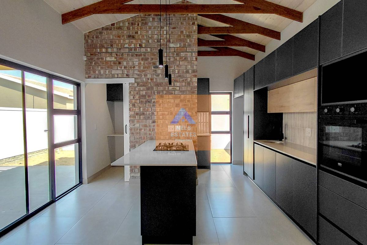 Modern kitchen featuring an exposed brick wall, timber roof trusses, a central island with a gas hob, and sleek dark cabinetry.