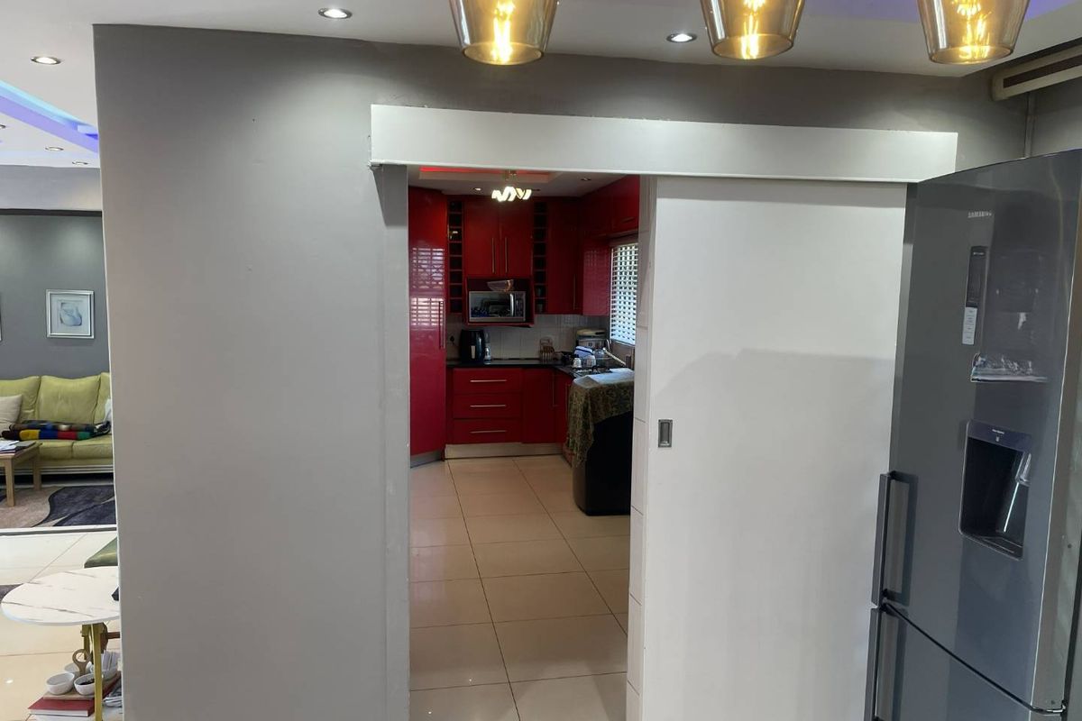 A view through a sliding door into a kitchen featuring red cabinetry, tiled floors, and recessed lighting, adjacent to a living area.