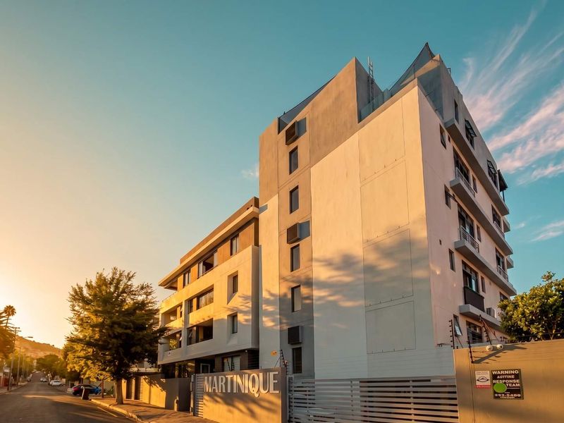 Exterior view of the Martinique apartment complex, featuring modern architectural design, balconies, and secure perimeter fencing at street level.