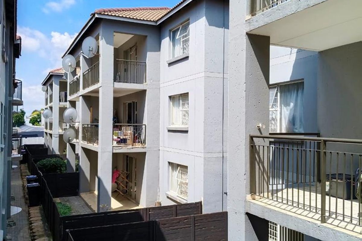 Exterior view of a multi-story townhouse complex featuring concrete balconies, metal railings, and small private garden spaces with paved walkways.