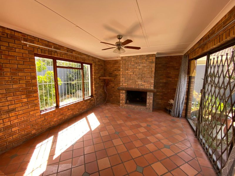 Enclosed patio area featuring exposed brick walls, a built-in brick fireplace, terracotta tile flooring, and a ceiling fan.