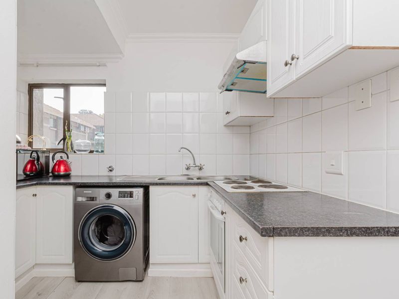 A functional kitchen featuring white cabinetry, dark laminate countertops, tiled backsplash, and integrated appliances including an oven, hob, and extractor fan.