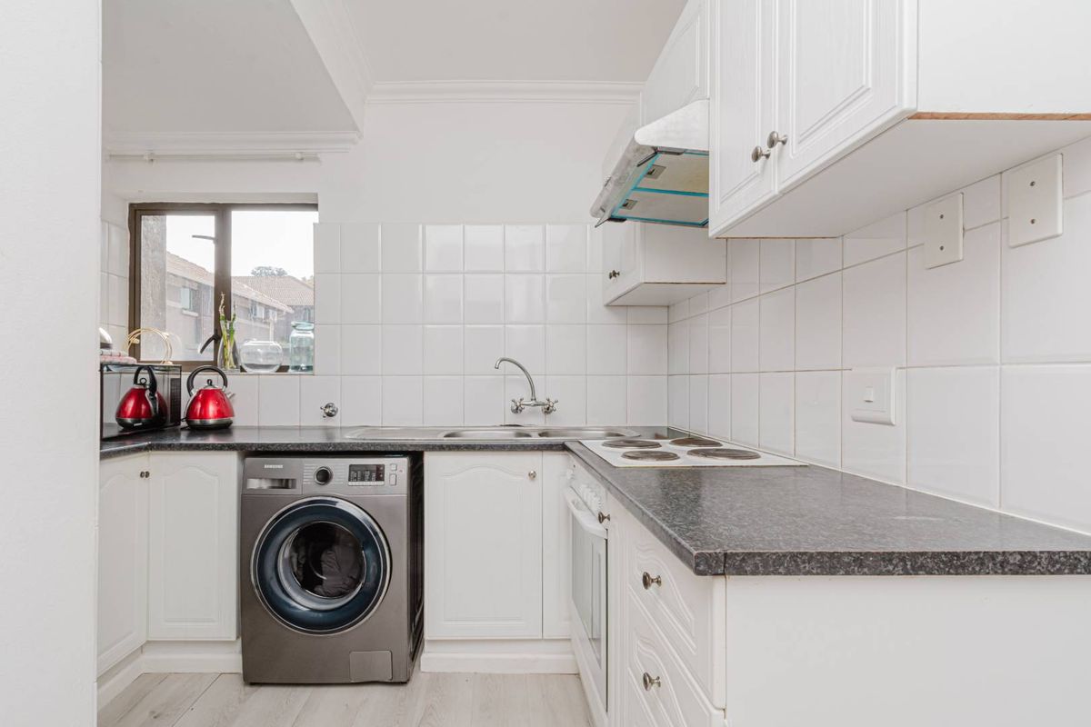 A functional kitchen featuring white cabinetry, dark laminate countertops, tiled backsplash, and integrated appliances including an oven, hob, and extractor fan.