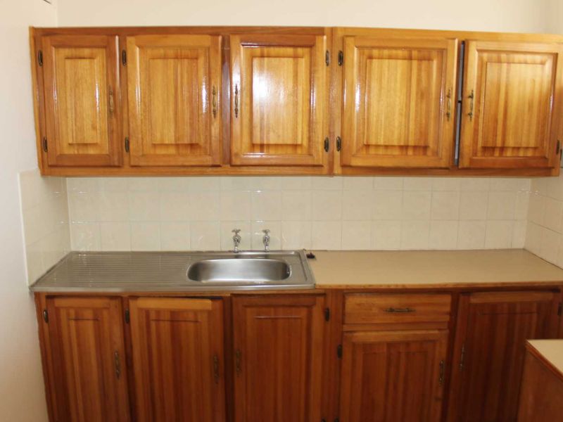 A functional kitchen area featuring traditional wooden cabinetry, a stainless steel sink, and a tiled splashback, offering a classic layout.