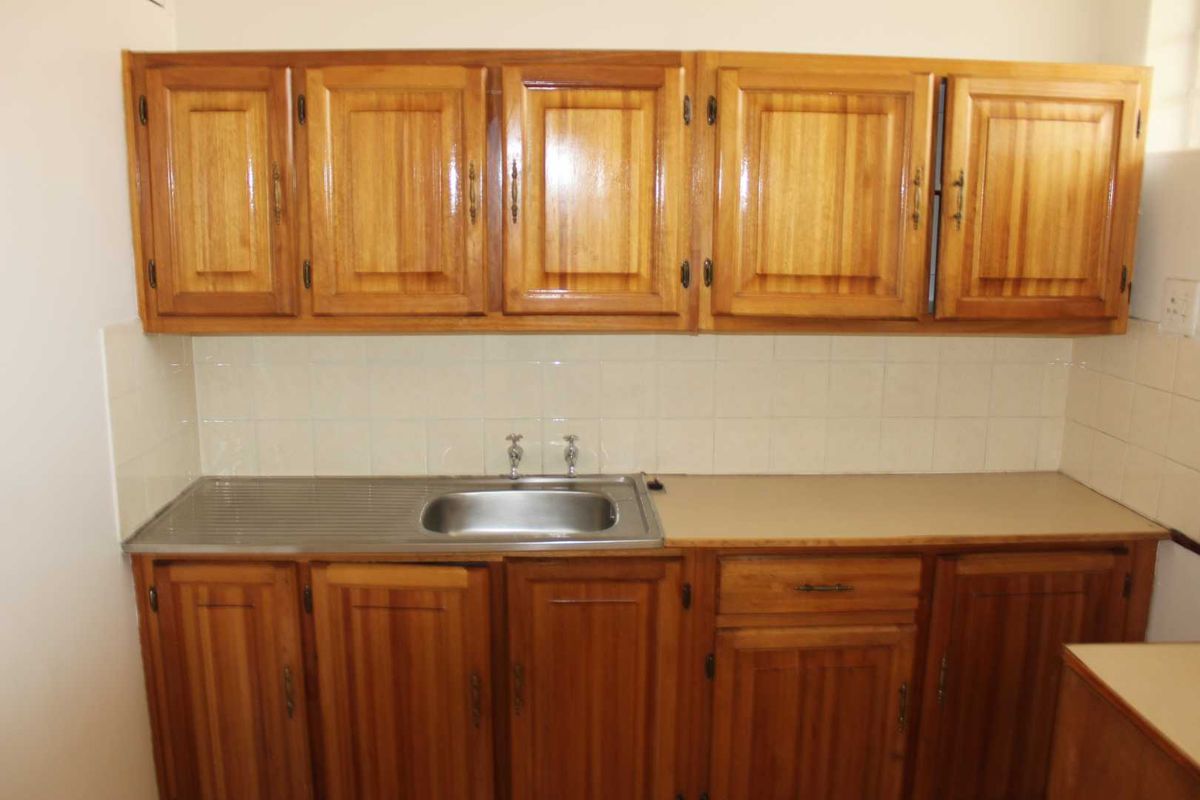 A functional kitchen area featuring traditional wooden cabinetry, a stainless steel sink, and a tiled splashback, offering a classic layout.