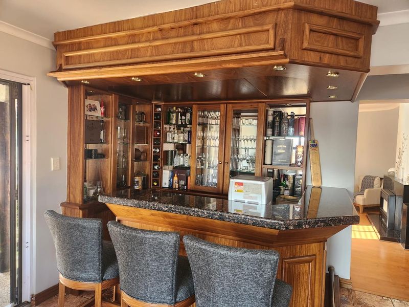 A well-maintained built-in wooden bar area featuring a granite countertop, integrated glass display cabinets, and recessed lighting.
