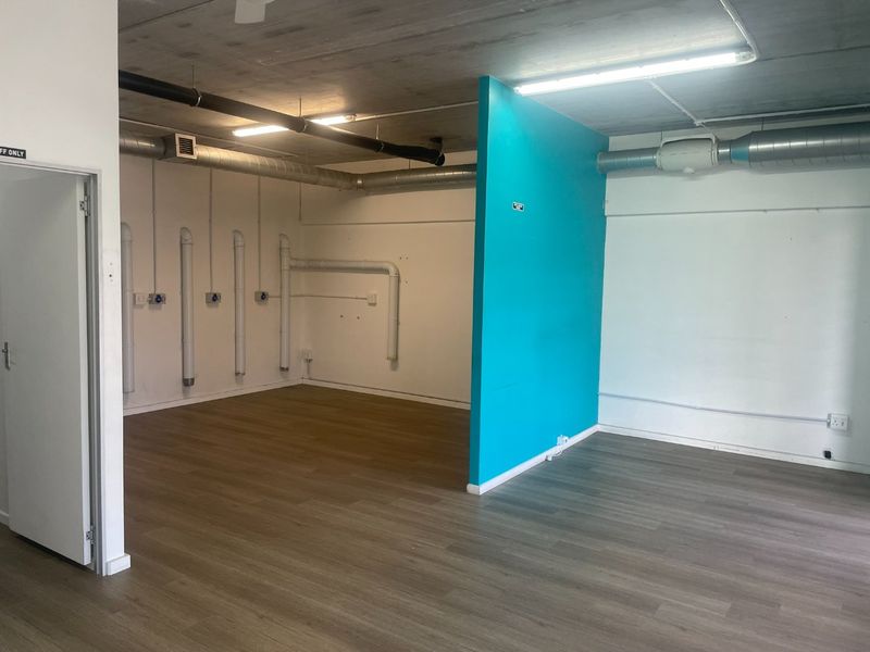 Open plan retail or office space featuring exposed industrial ceilings, ducting, vinyl flooring, and a vibrant blue partition wall.