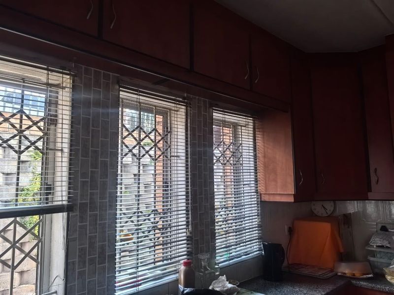 A kitchen area featuring dark wood cabinetry, tiled backsplash, and windows fitted with security bars and venetian blinds.