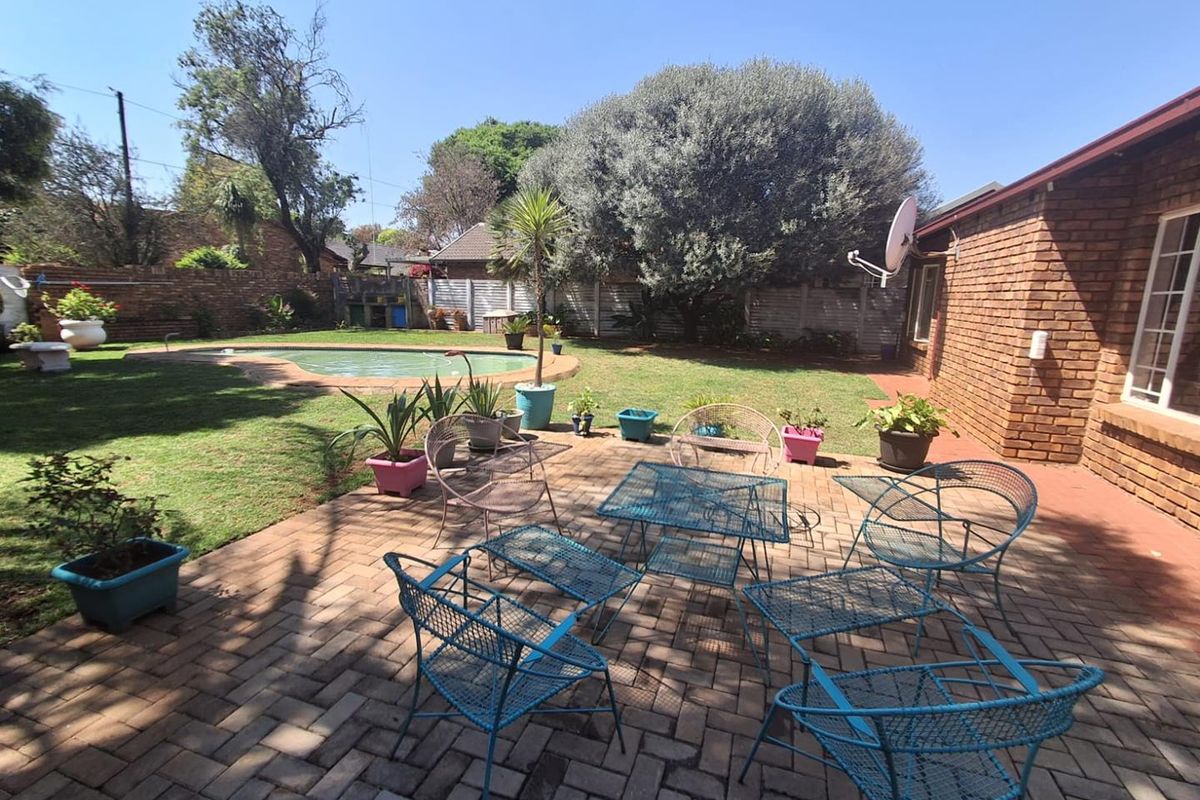 Spacious rear garden featuring a swimming pool, paved patio area, and established trees, providing a private outdoor space for relaxation and entertainment.