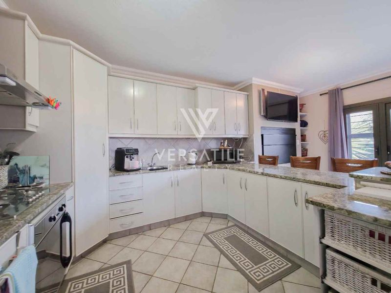 A functional kitchen featuring ample built-in cabinetry, granite countertops, a gas hob with extractor fan, and a breakfast nook area with tiled flooring.