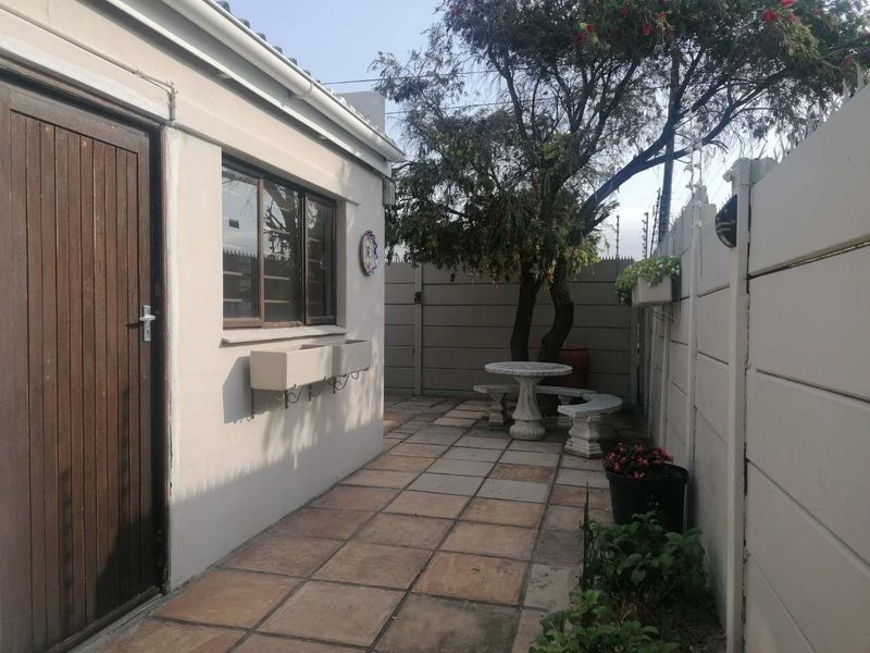 A private rear courtyard featuring tiled flooring, a precast concrete boundary wall, and direct access to the property via a timber door.