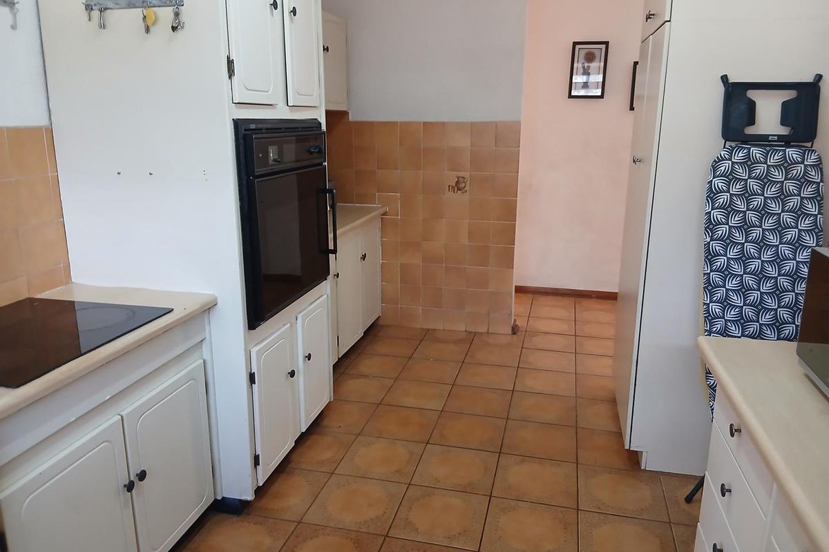 A dated kitchen featuring tiled flooring, built-in cabinetry, and a wall-mounted oven, offering a functional layout with potential for modernization.