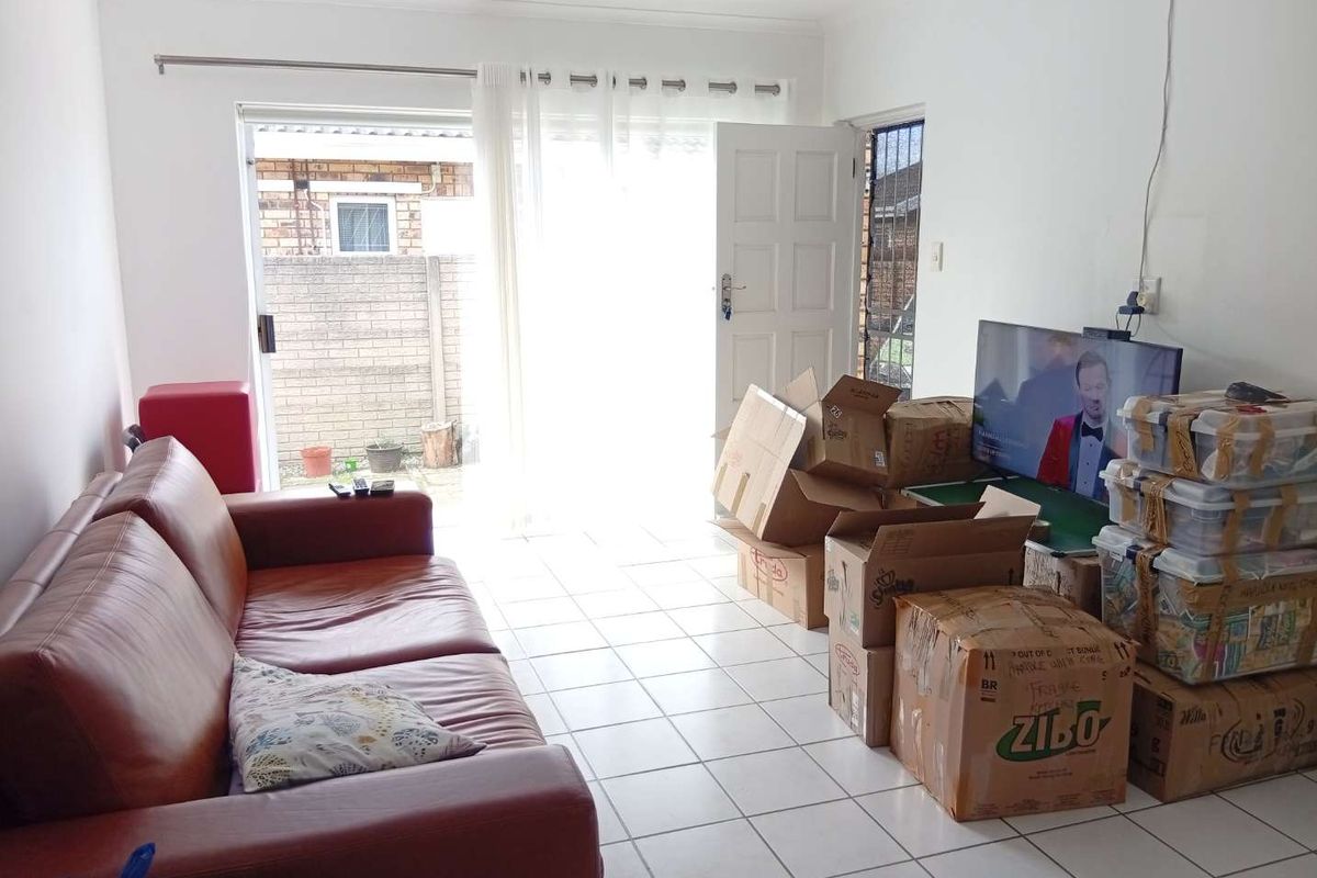 A living room featuring tiled flooring and a sliding glass door providing access to the exterior, currently used for storage.