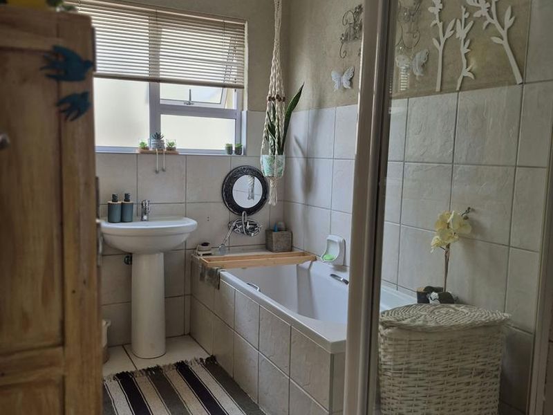 A functional bathroom featuring a pedestal basin, a built-in bathtub, and a separate shower enclosure with neutral wall and floor tiling.
