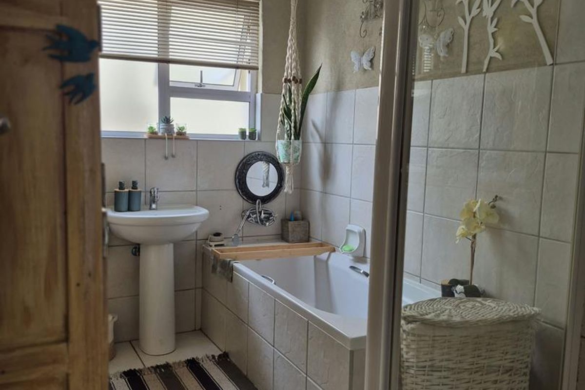 A functional bathroom featuring a pedestal basin, a built-in bathtub, and a separate shower enclosure with neutral wall and floor tiling.