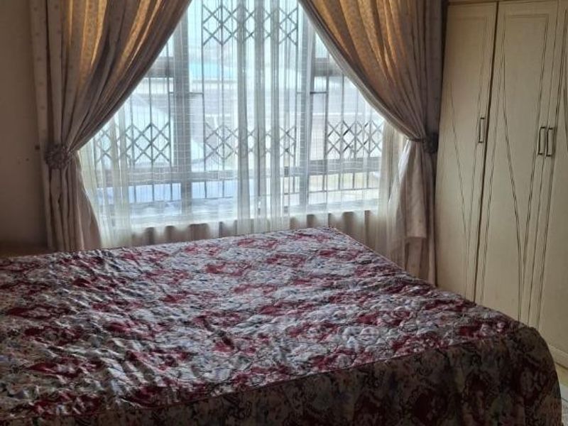 A bedroom featuring built-in wardrobes, tiled flooring, and a window fitted with a security gate.