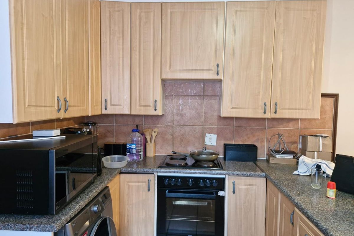 A functional kitchen featuring light wood-finish cabinetry, granite-look countertops, a built-in oven with a hob, and tiled splashbacks.
