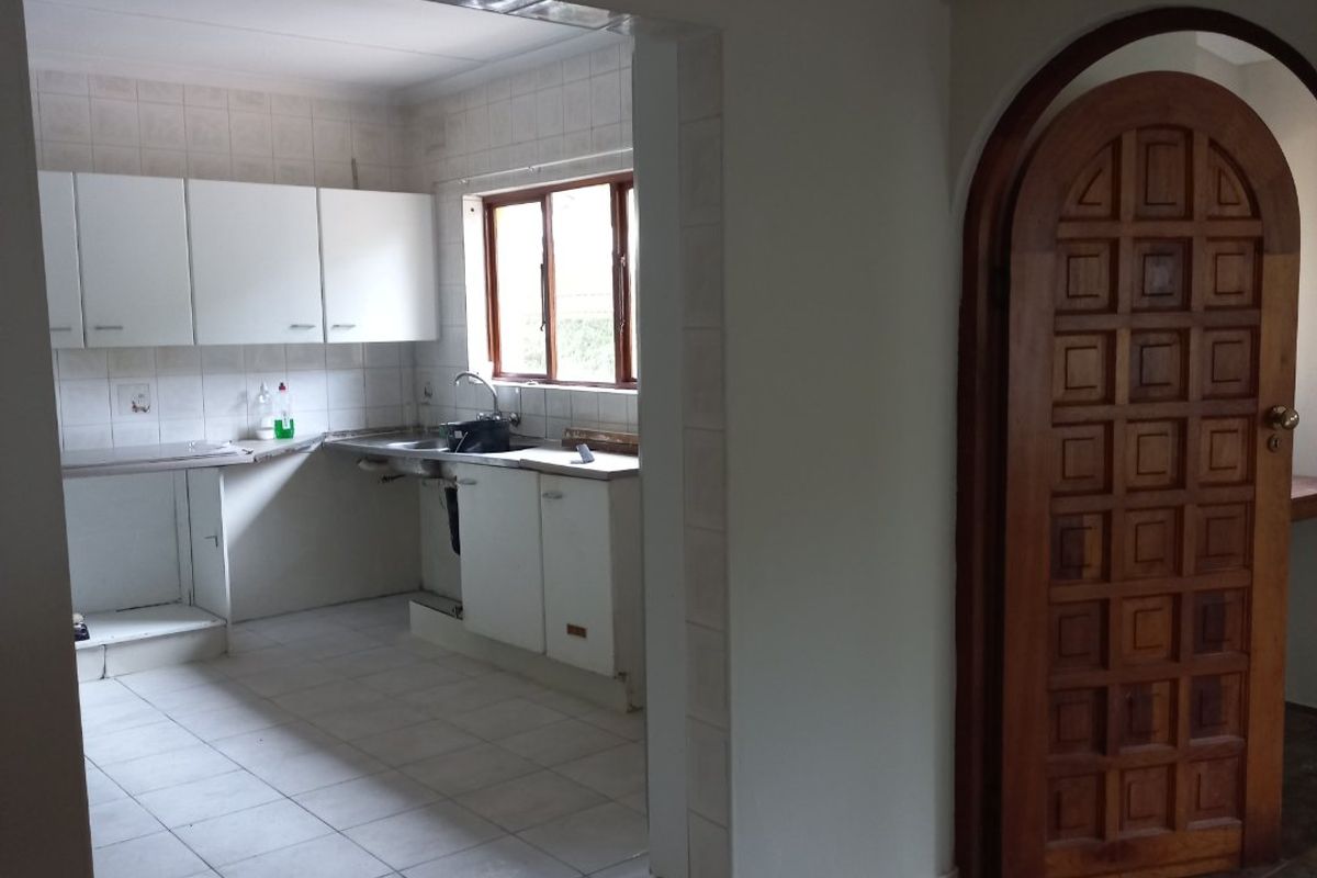 A dated kitchen featuring white cabinetry, tiled backsplash, and tiled flooring, adjacent to an arched wooden doorway leading to another area.