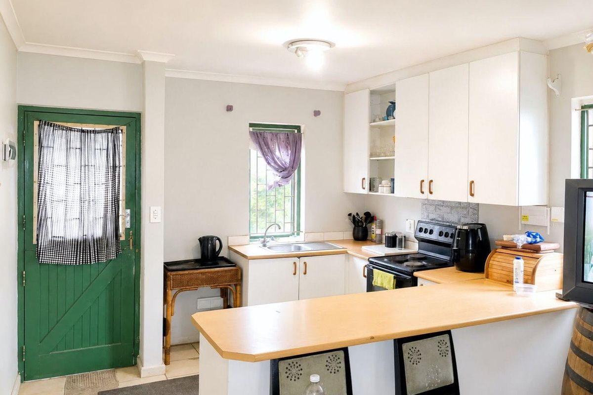 A functional kitchen featuring white cabinetry, laminate countertops, a stainless steel sink, and a breakfast bar, with direct access to an exterior door.