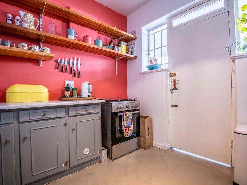 Kitchen featuring grey cabinetry, open wooden shelving, a freestanding stove, and a security door leading to the exterior.