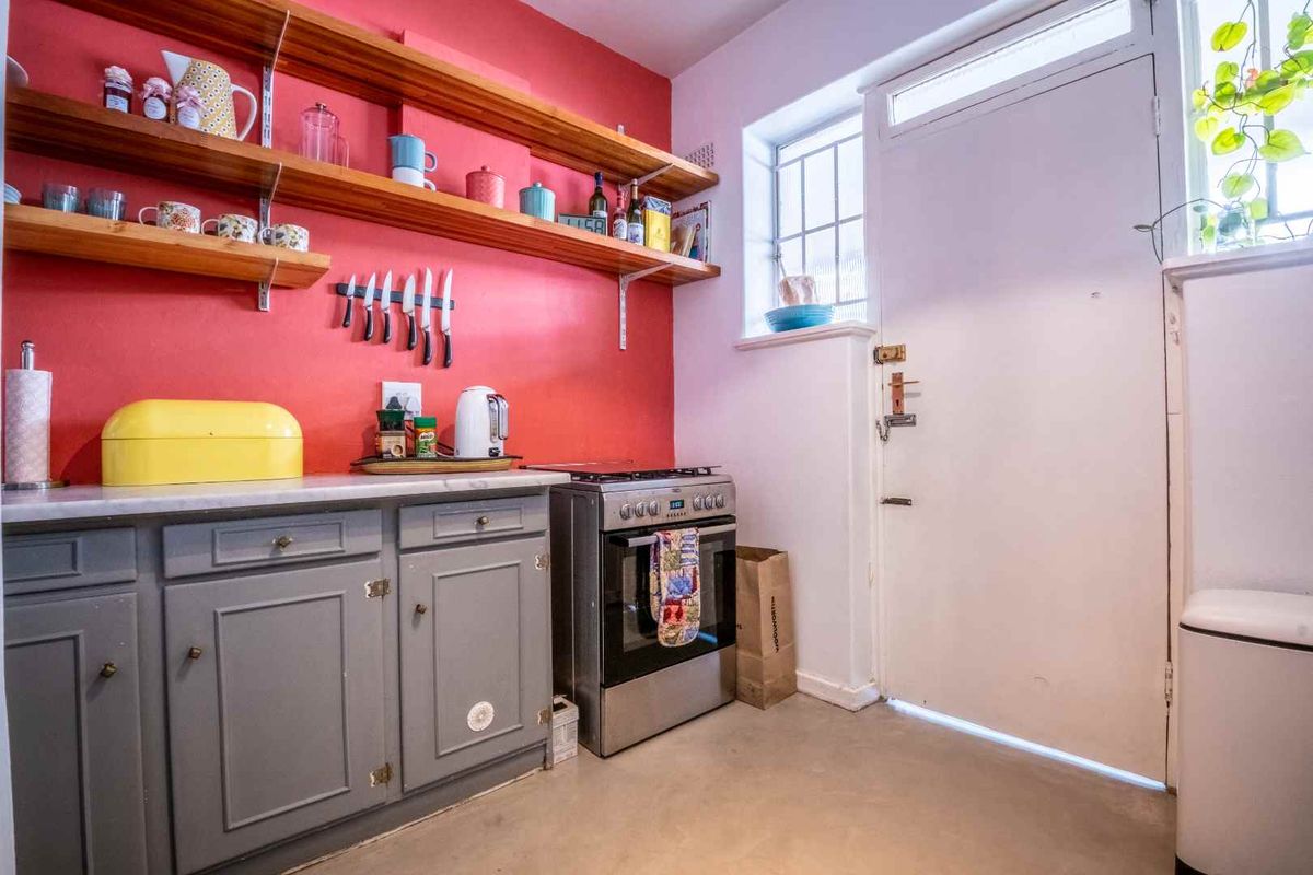 Kitchen featuring grey cabinetry, open wooden shelving, a freestanding stove, and a security door leading to the exterior.