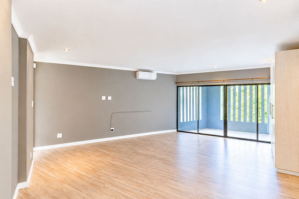 Spacious, light-filled living area featuring modern laminate flooring, built-in cabinetry, air conditioning, and large sliding glass doors leading to an outdoor space.