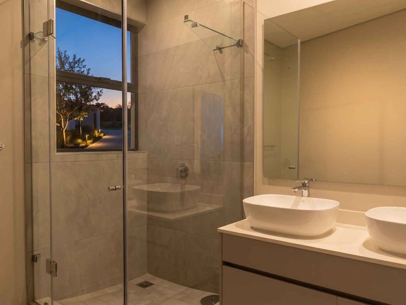 Modern bathroom featuring a double vanity with vessel sinks, a glass-enclosed shower, and large wall-mounted mirror with contemporary finishes.