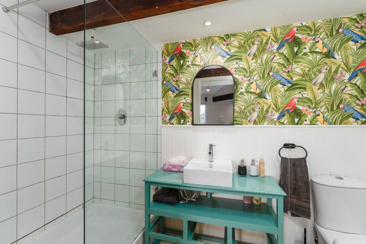 A well-maintained bathroom featuring a glass-enclosed walk-in shower, a modern vessel sink vanity, and vibrant tropical-themed wallpaper.