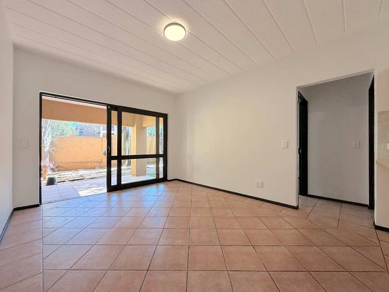 An empty living room featuring tiled flooring, a textured ceiling, and a large sliding glass door providing access to an outdoor patio area.