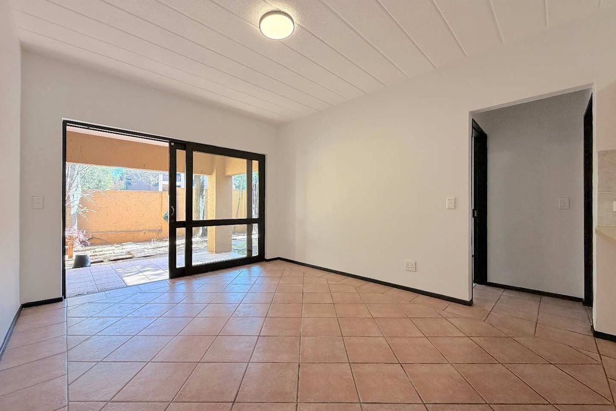 An empty living room featuring tiled flooring, a textured ceiling, and a large sliding glass door providing access to an outdoor patio area.