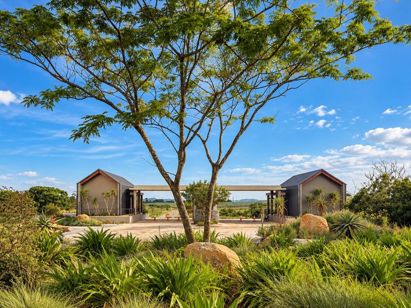 A well-maintained modern gated entrance featuring landscaped gardens, stone accents, and paved driveway leading into the residential estate.
