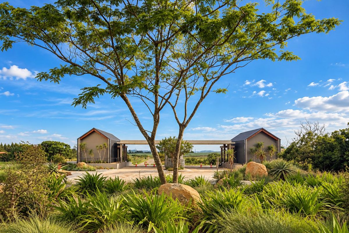 A well-maintained modern gated entrance featuring landscaped gardens, stone accents, and paved driveway leading into the residential estate.