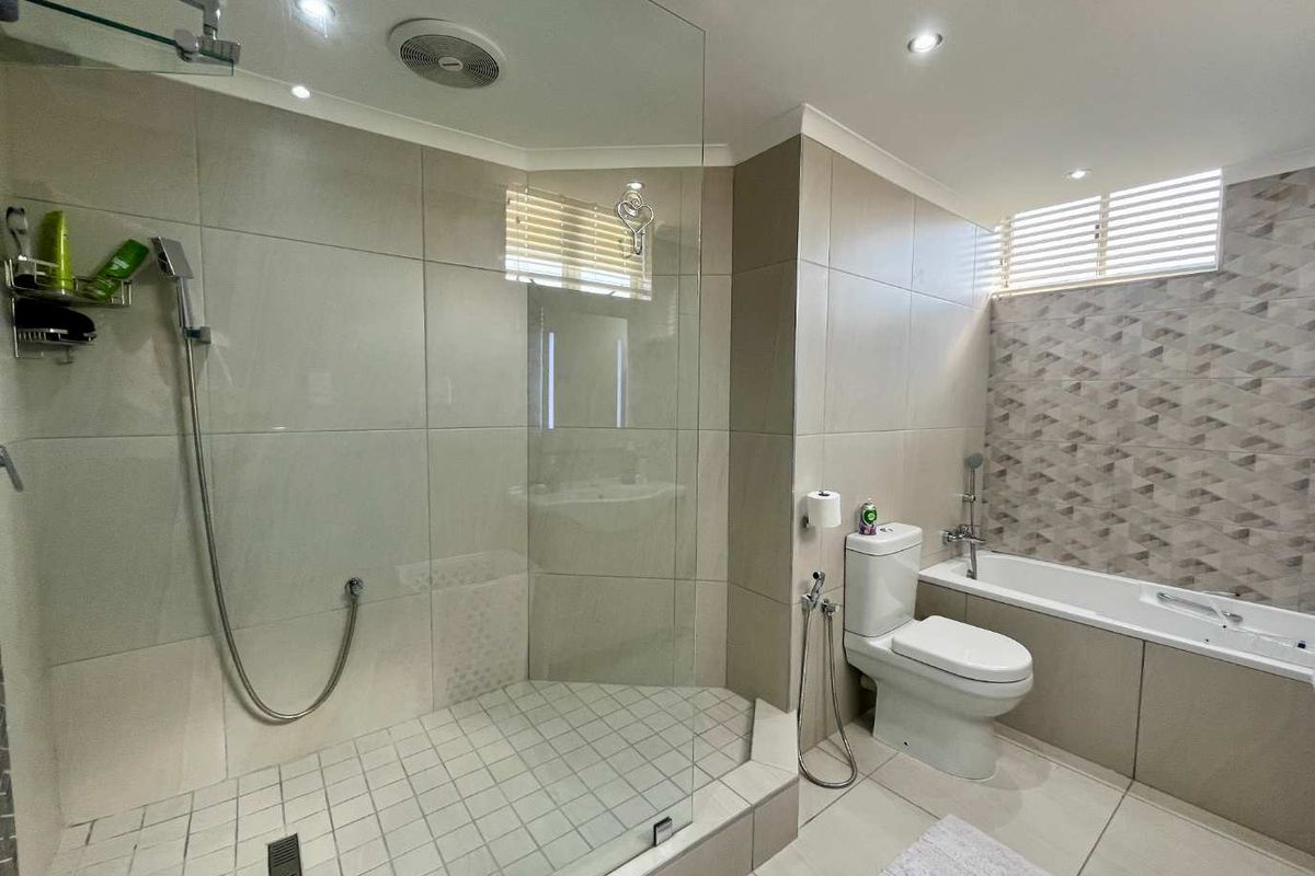 Modern bathroom featuring a glass-enclosed walk-in shower, a separate bathtub, and neutral wall tiling with a decorative accent wall.
