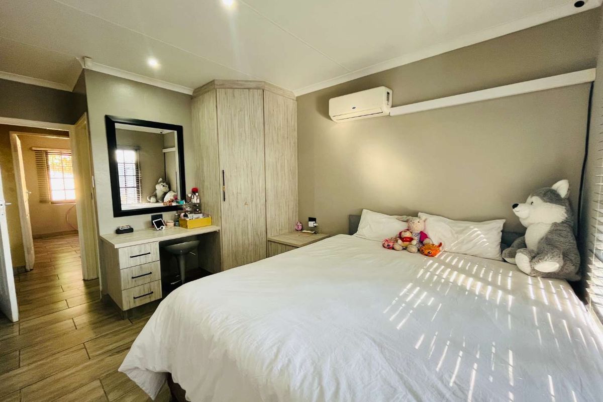 A well-maintained bedroom featuring built-in wooden cabinetry, a vanity unit, tiled flooring, and a wall-mounted air conditioning unit.