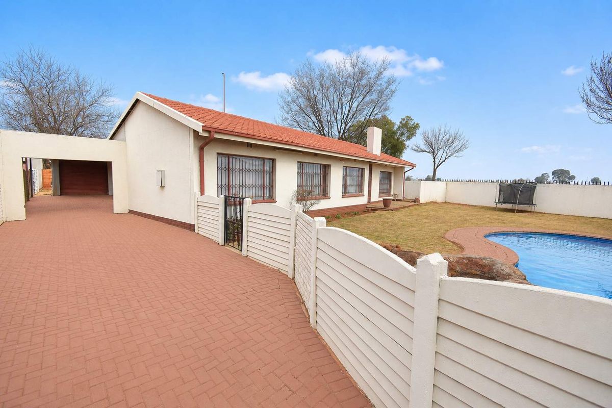 Rear view of the property featuring a paved driveway, swimming pool, and a well-maintained garden with boundary walling.