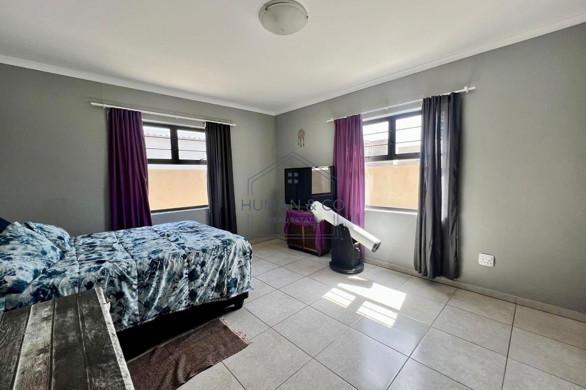 A spacious bedroom featuring neutral tiled flooring, large windows with curtain rods, and a central ceiling light fixture.