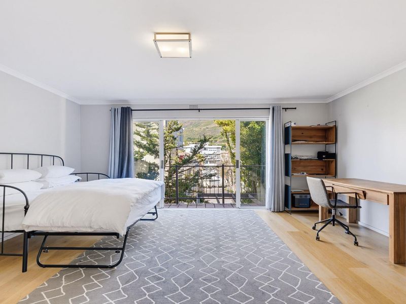A bright and spacious bedroom featuring hardwood flooring, a ceiling light fixture, and large sliding glass doors that open onto a private balcony.