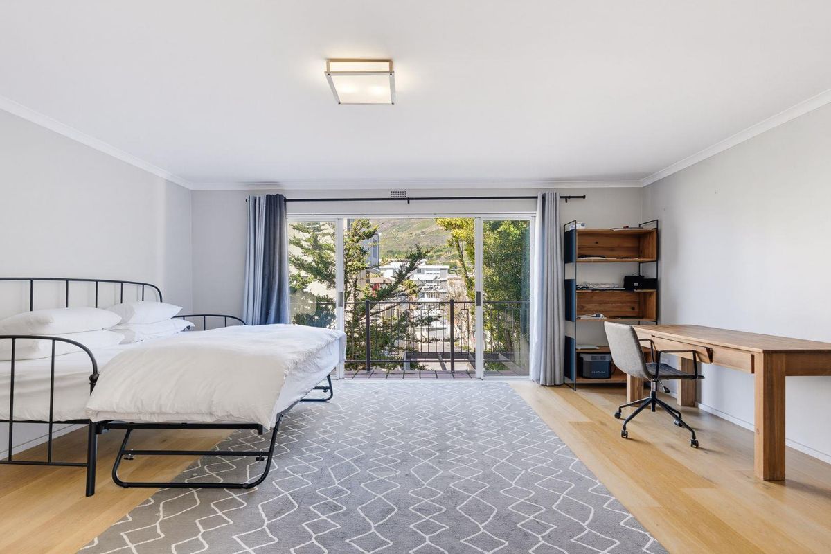 A bright and spacious bedroom featuring hardwood flooring, a ceiling light fixture, and large sliding glass doors that open onto a private balcony.