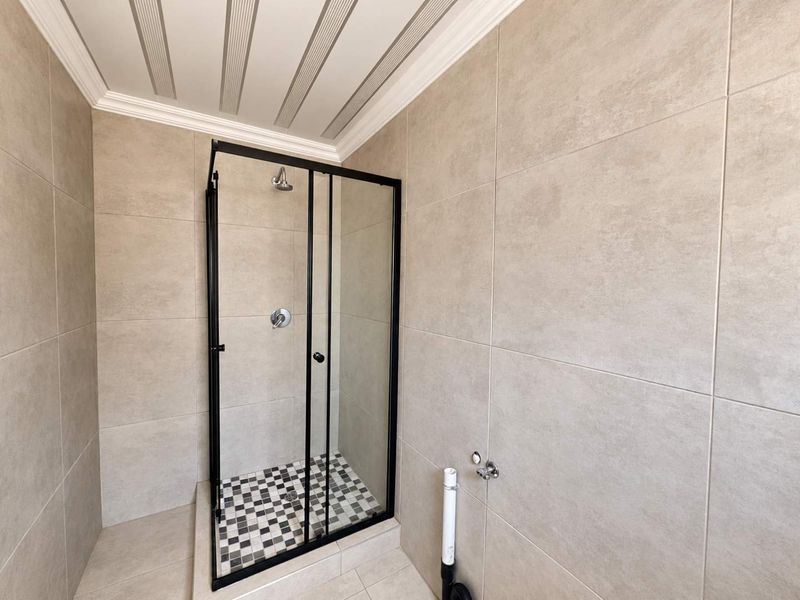 A modern bathroom featuring a glass shower enclosure with black framing, neutral wall tiling, and a decorative mosaic tiled shower floor.