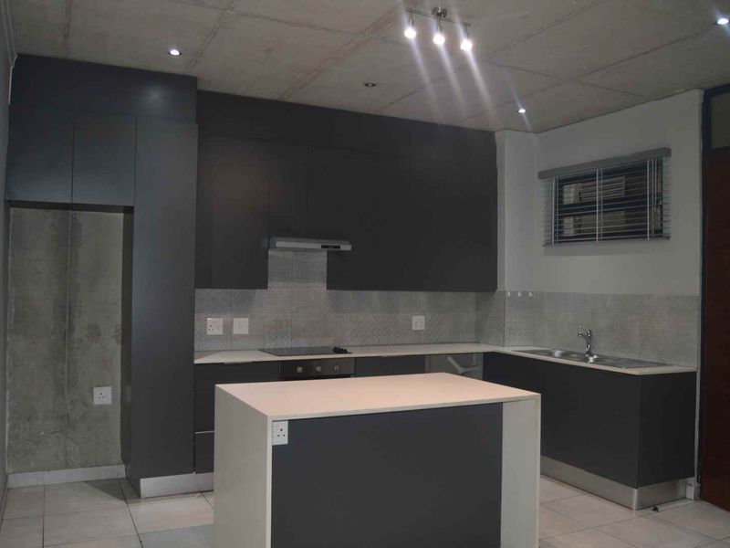 Modern kitchen featuring dark grey cabinetry, a central island, built-in oven and hob, and a double sink with tiled backsplash.