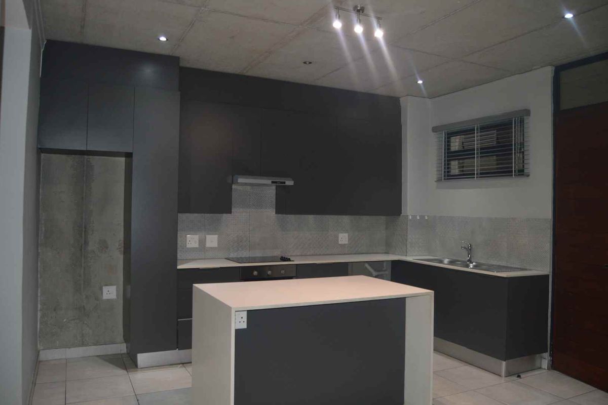 Modern kitchen featuring dark grey cabinetry, a central island, built-in oven and hob, and a double sink with tiled backsplash.